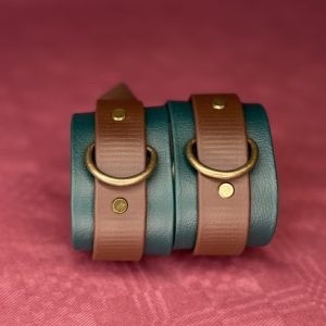 Grün-braune Biothane Cuffs vor rotem Hintergrund, stehend nebeneinander