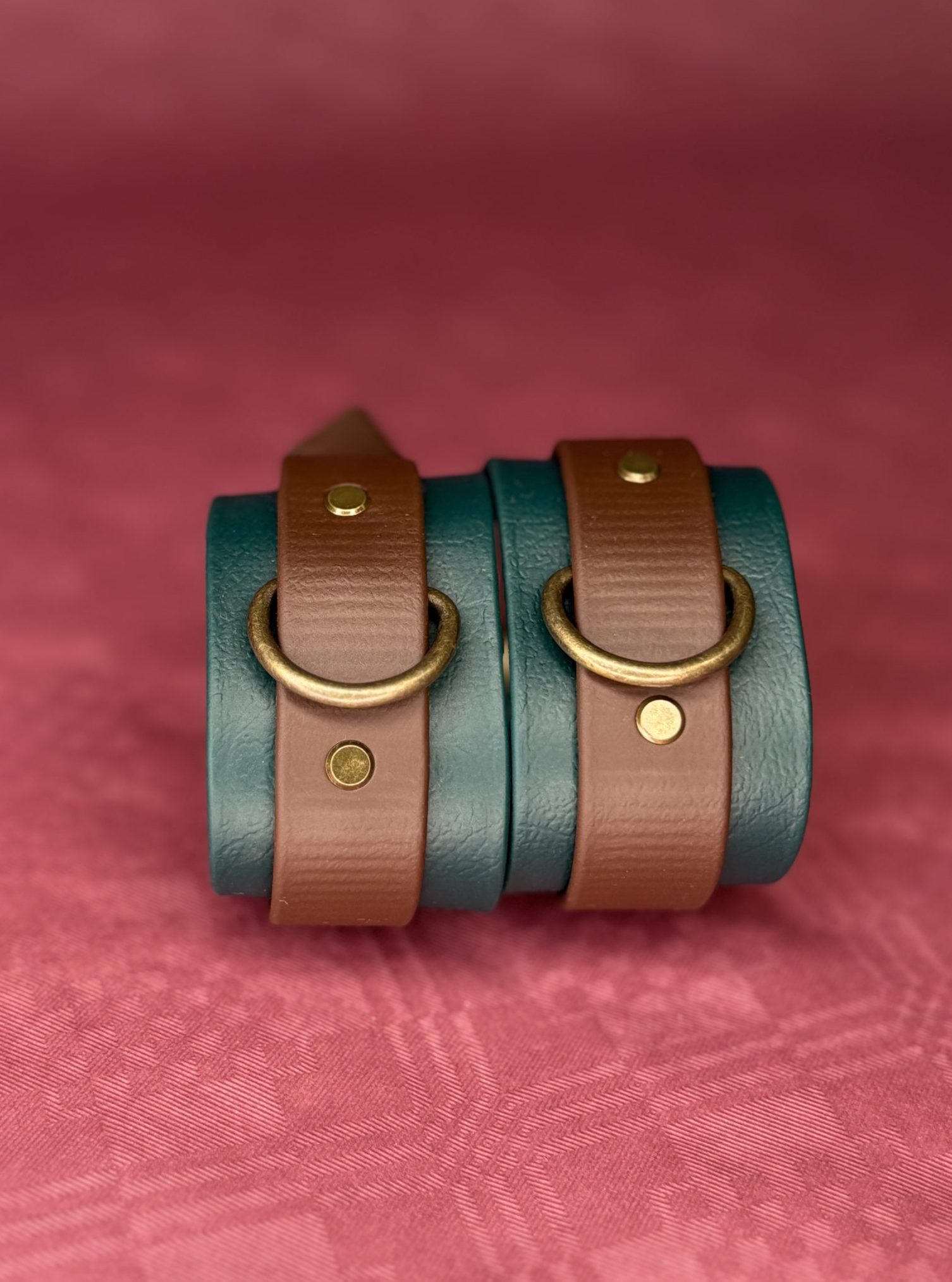 Grün-braune Biothane Cuffs vor rotem Hintergrund, stehend nebeneinander